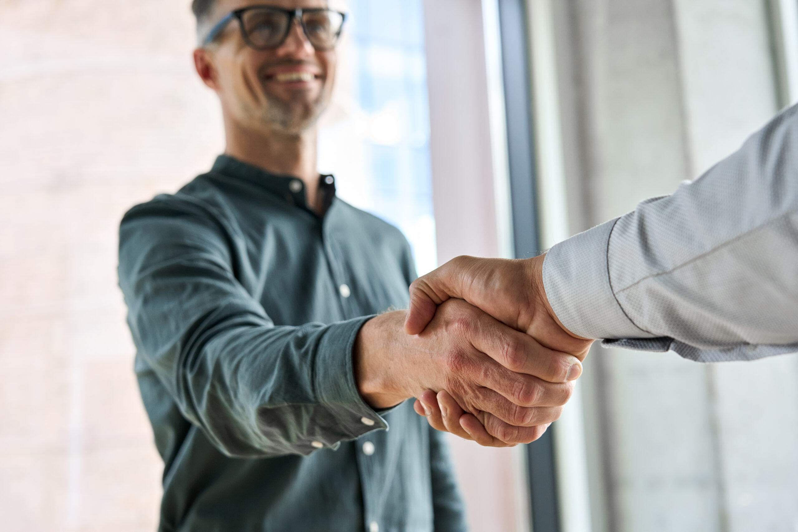 Two professionals shaking hands in a formal office setting, symbolising a successful business deal.