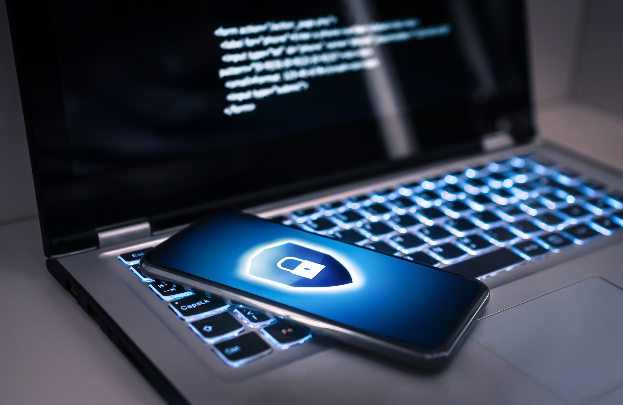 A locked smartphone placed on a laptop keyboard, illuminated by a blue light.